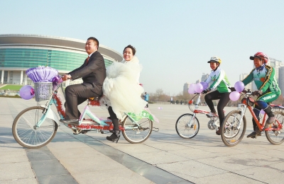 氣球和鮮花裝點(diǎn)的雙人自行車，新郎郝幸福載著美麗新娘回家。