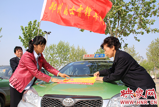 　　授旗結(jié)束后，首都的士雷鋒車隊王鳳進隊長（右）與鄭州的的哥的姐在車身上貼上標(biāo)識。