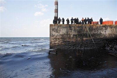 昨日，山東青島，清污人員正在海邊清理油污。