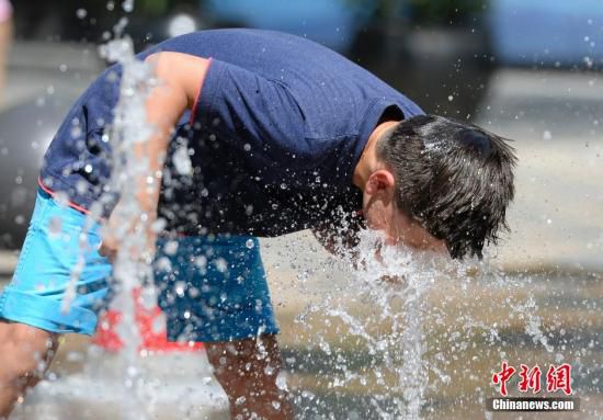 5月29日，一名小孩將頭伸向北京街頭的噴泉以降溫祛暑。