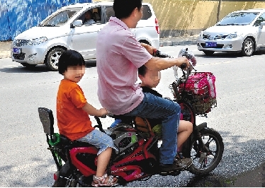 周先生騎著一輛低矮的電動車帶著一對兒女，很不安全。