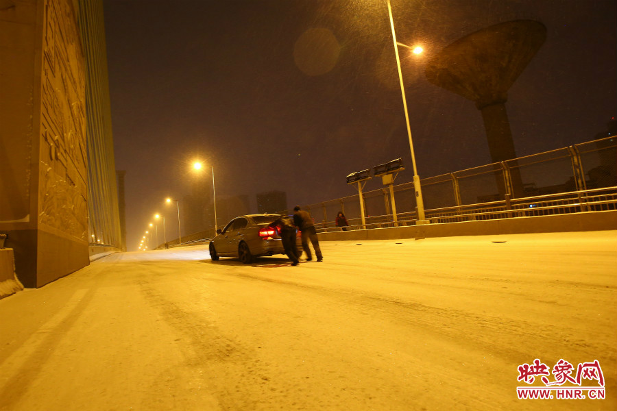 雪天路滑，汽車(chē)上橋打滑，兩名“推車(chē)人”幫助一輛私家車(chē)上坡。