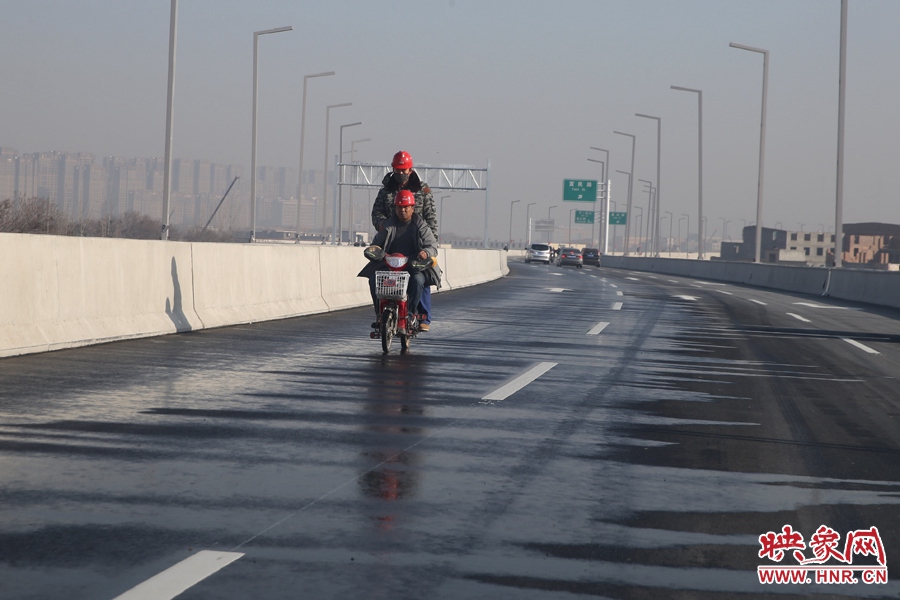 兩名工人騎車經(jīng)過灑水養(yǎng)護(hù)路面。